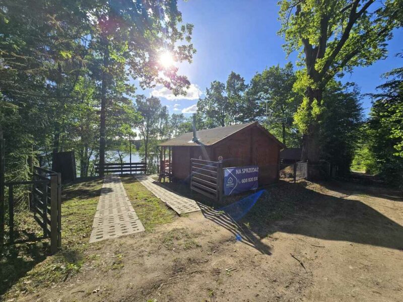 Działka rekreacyjna z domkiem i linią brzegową jeziora.